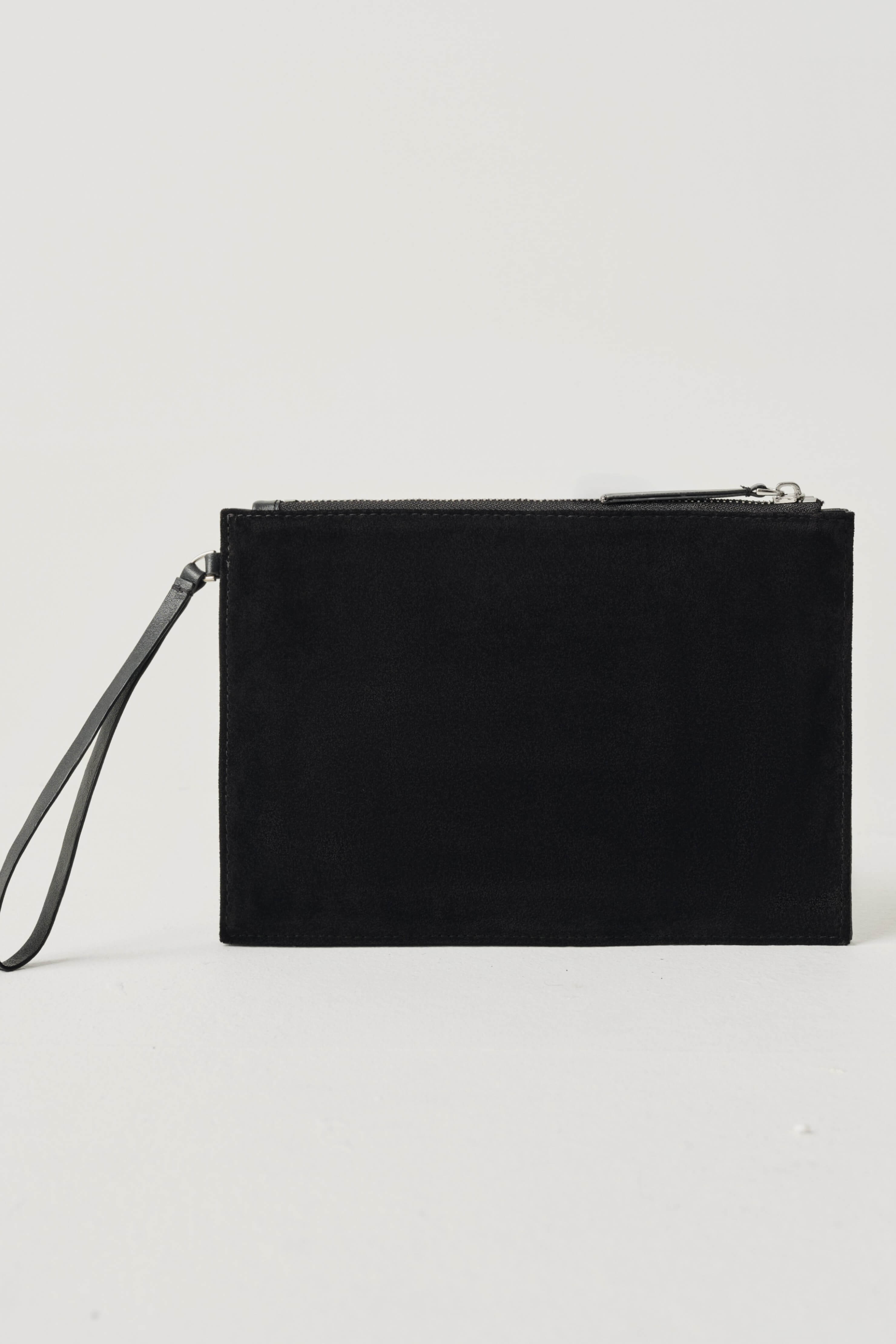 A black suede wristlet clutch with a top zipper and a matching black wrist strap, photographed on a clean, light gray studio background.