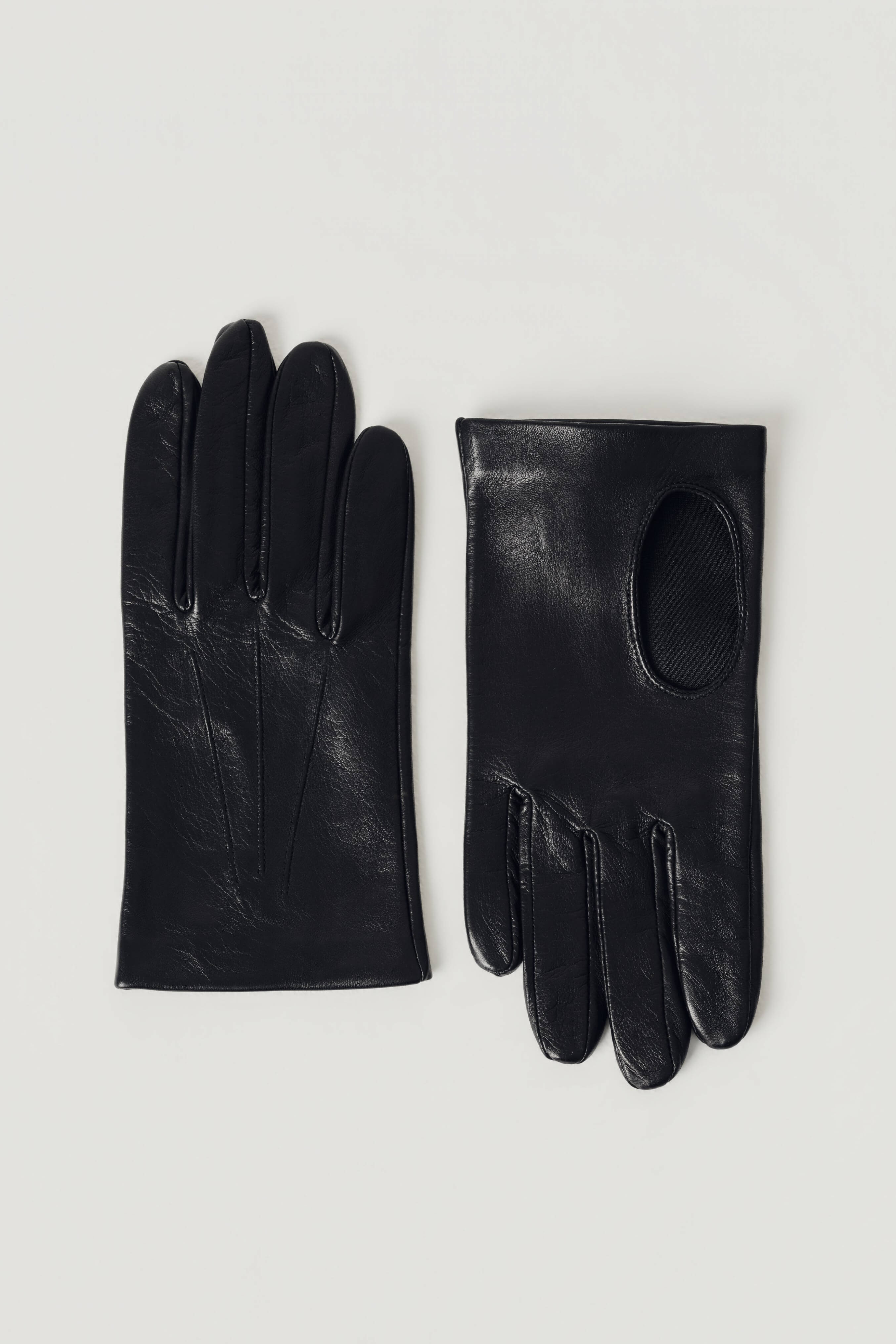A pair of black leather gloves, one showing the back of the hand with finger seams and the other showing the palm with a circular cutout, laid flat on a light gray background.