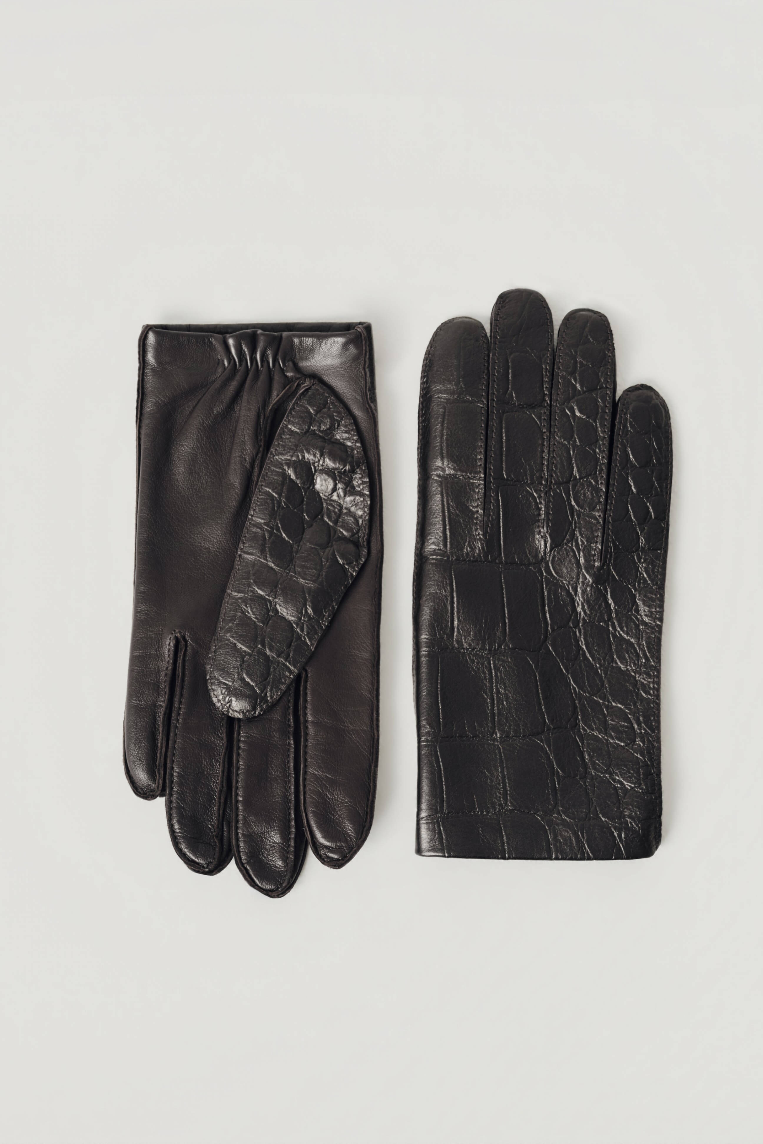 A pair of black leather gloves, one showing the smooth back of the hand and the other showing the crocodile-embossed palm, laid flat on a light gray background.