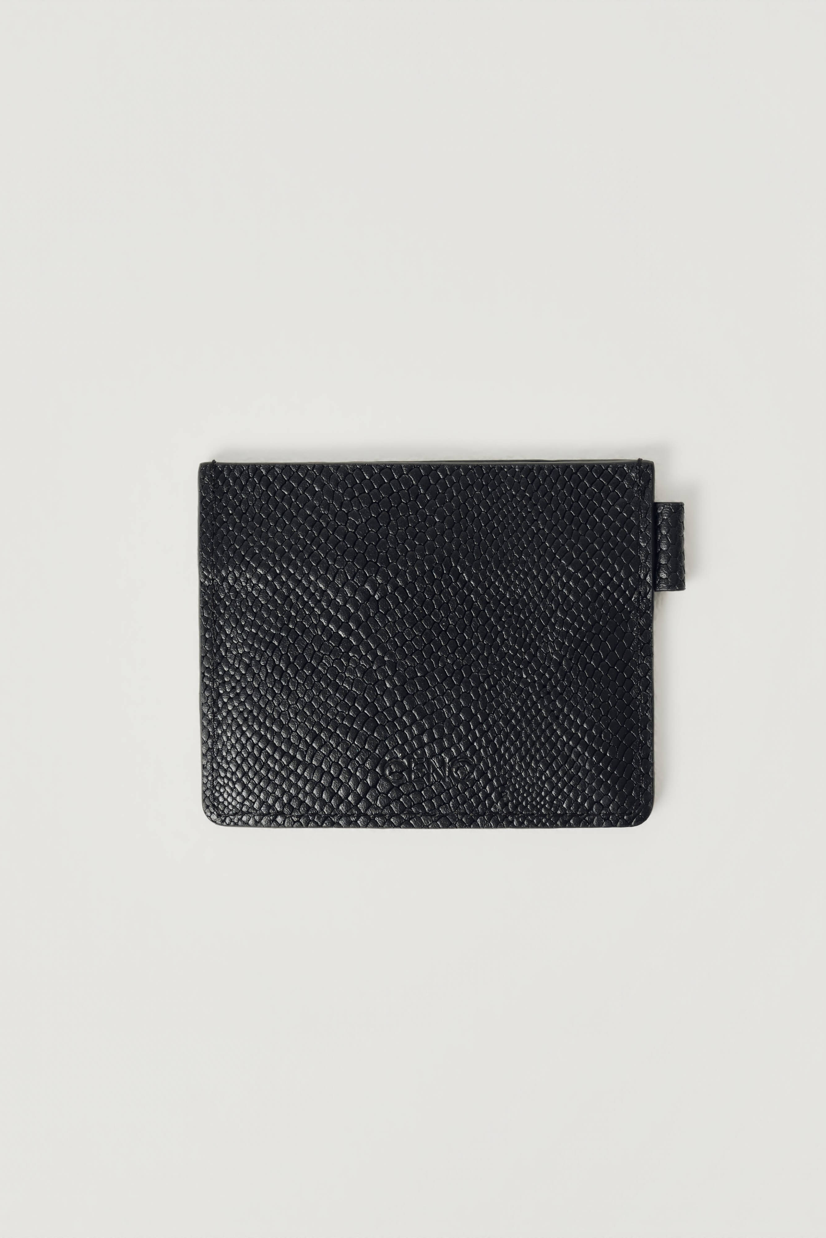 A black textured leather wallet with a small black fabric tab on the right side, photographed flat against a light gray background.